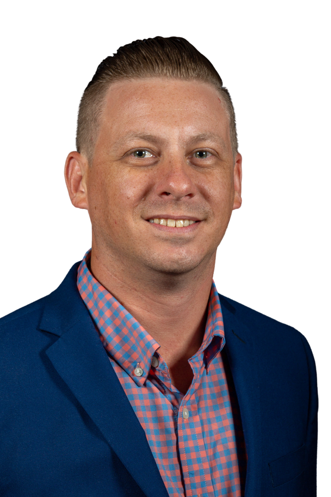 A man with short hair, wearing a blue blazer and a pink and blue checkered shirt, smiles at the camera against a black background.