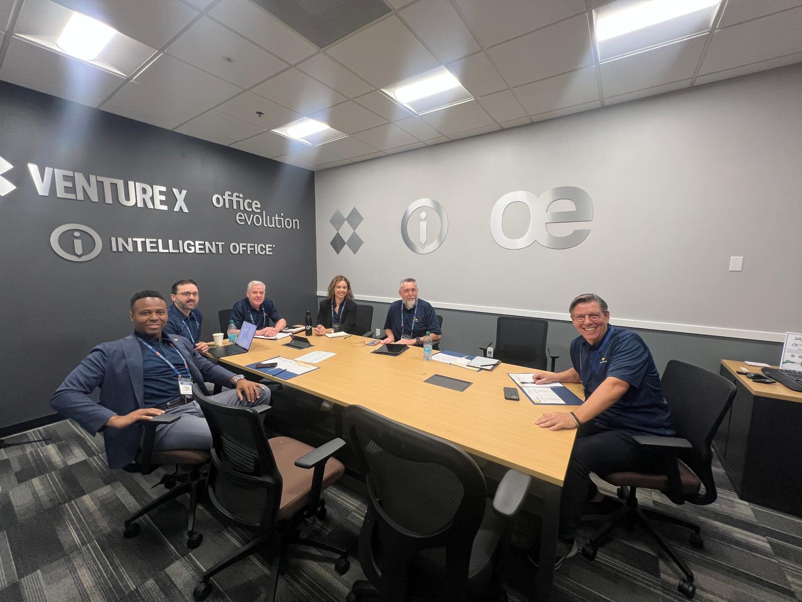 Three business professionals in suits are looking at a tablet screen together in an office setting.
